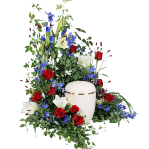 Vit urna omgiven av röda rosor, vita liljor och blå blommor.